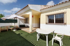 Une terrasse avec une table et des chaises, un banc et un espace abrité avec un parasol.