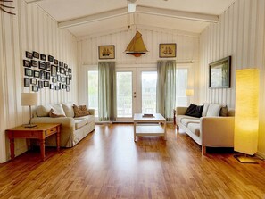 A spacious living room with wooden flooring, two sofas, a coffee table, and a wall adorned with framed pictures. - Blue Anchor Charming Beach Cottage. Short Walk to  Beach, North Litchfield (Pawleys Island)