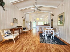 A spacious living area with a wooden floor, white furniture, a dining table with chairs, a ceiling fan, and a kitchen in the background. - Blue Anchor Charming Beach Cottage. Short Walk to  Beach, North Litchfield (Pawleys Island)