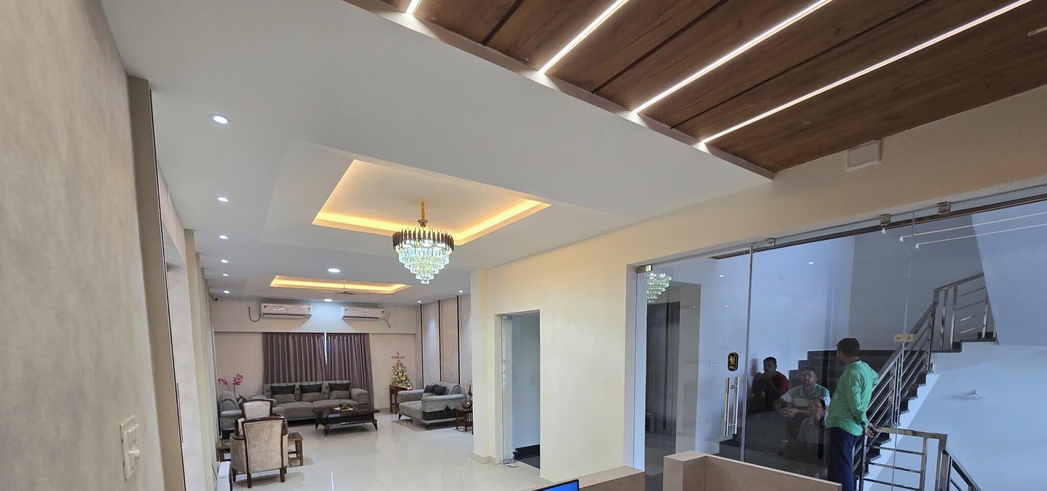 A spacious living area with a modern chandelier, a sofa set, and a glass door leading to a staircase.