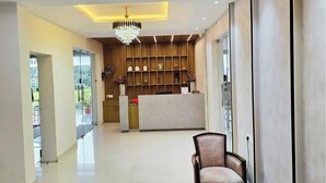 Un hall de hotel con mostrador de recepción, una araña de cristal, una mesa de centro de vidrio y una zona de recepción de madera.