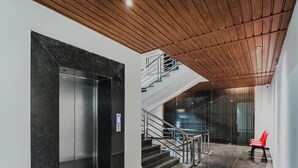 Un interior con un ascensor moderno, una escalera y un techo de madera.