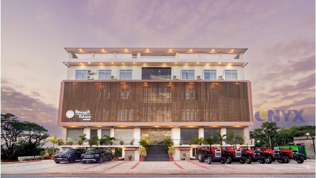 Un edificio moderno con un letrero que dice 'Binouah Palace' y una fila de vehículos estacionados al frente.