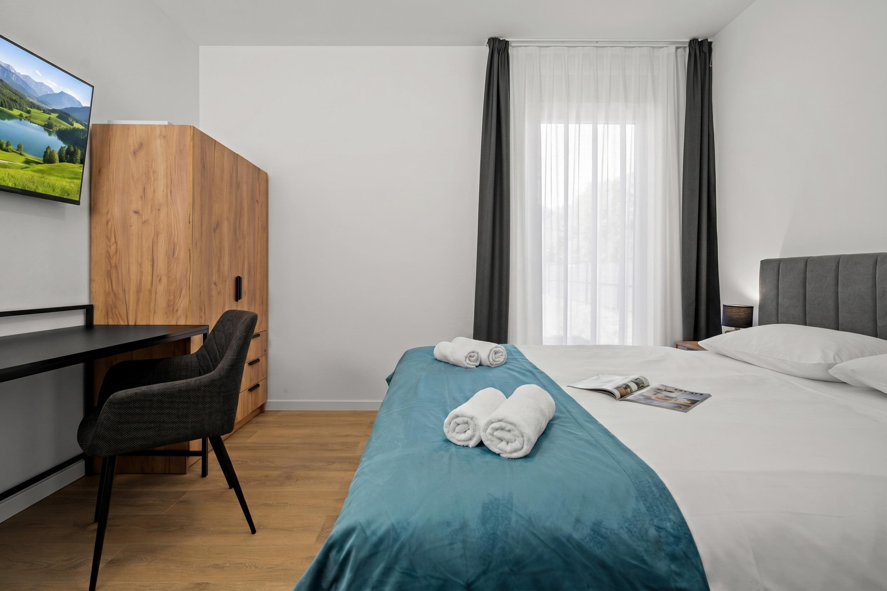 A hotel room with a bed, a desk, a chair, and a TV on the wall.