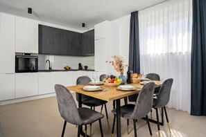 A modern kitchen with dark cabinets, a built-in oven, and a dining area with a wooden table set for four. - Villa Vallis (Sveta Nedelja)
