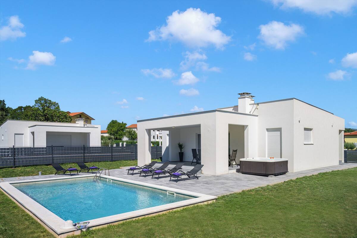 Una casa moderna con piscina, sillas de descanso y bañera de hidromasaje.