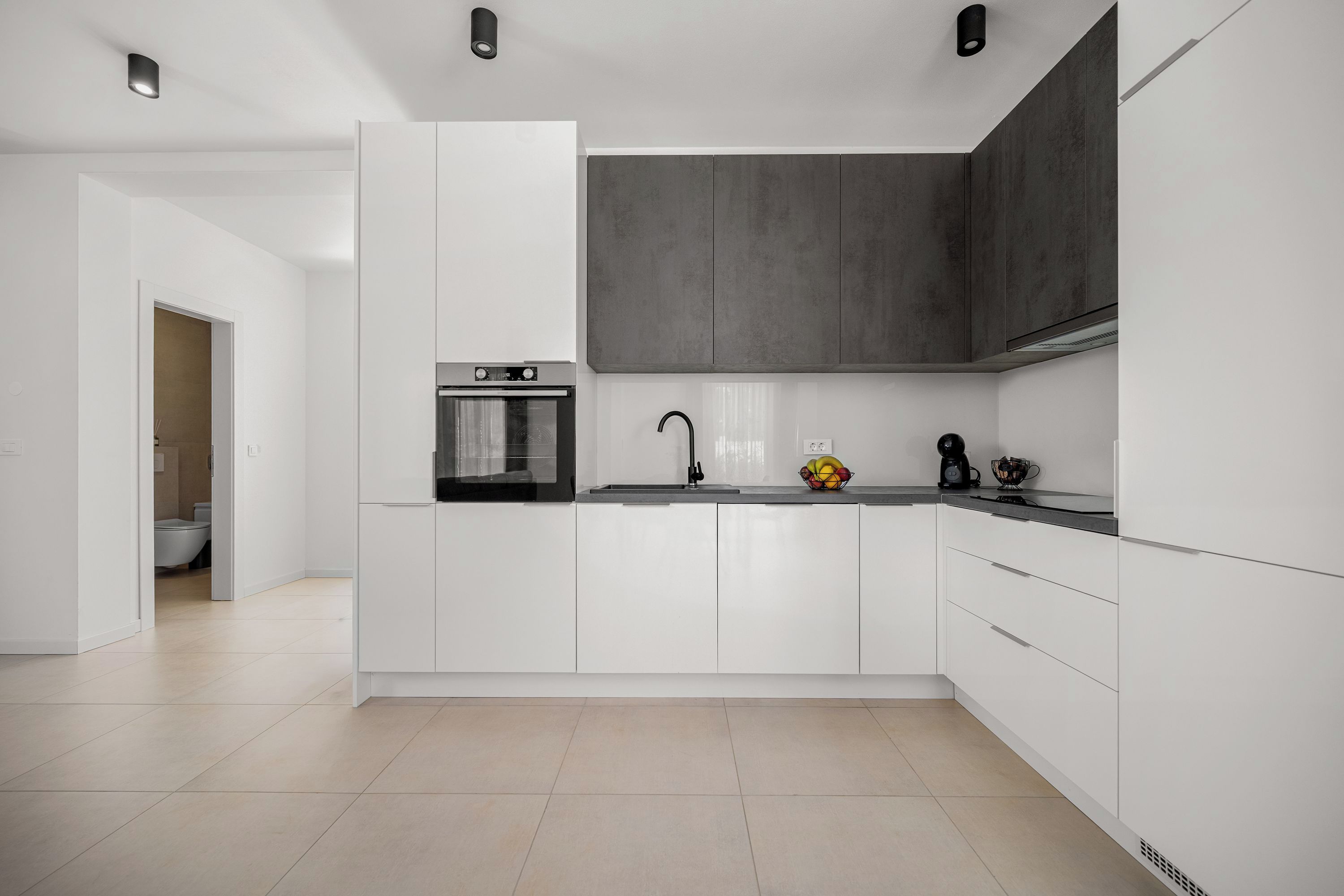 A modern kitchen with white cabinetry, a built-in oven, and a black faucet.