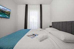 A hotel room with a bed, a flat-screen TV, a window with curtains, and a view of mountains. - Villa Vallis (Sveta Nedelja)