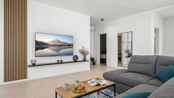Uma sala de estar moderna com televisão de tela plana, um sofá cinza, uma mesa de centro com uma bandeja de muffins e um painel de parede em ripas de madeira.