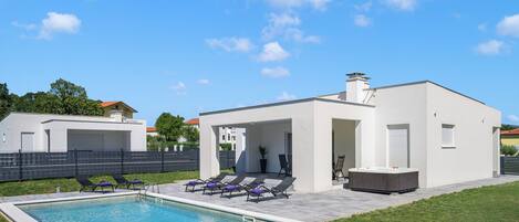 A modern house with a swimming pool, lounge chairs, and a hot tub.