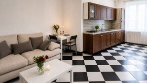 A modern living room with a sofa, a dining table, and a kitchen area with wooden cabinets and a checkered floor. - Centro Storico Savona - Porto Crociere 2 (Savona)