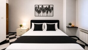 A modern hotel room with a black and white checkered floor, a bed with black and white bedding, a bedside table with a lamp, and a wall-mounted artwork. - Centro Storico Savona - Porto Crociere 2 (Savona)