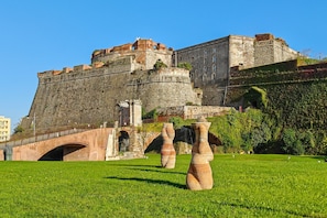 Una fortaleza de piedra histórica con un puente, esculturas de terracota y un campo cubierto de césped.