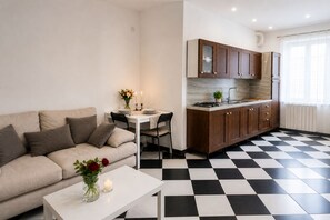 A modern living room with a sofa, a dining table, and a kitchen area with wooden cabinets and a checkered floor. - Centro Storico Savona - Porto Crociere 2 (Savona)
