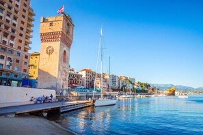 A coastal cityscape with a prominent clock tower, a marina with boats, and a variety of buildings along the waterfront. - Centro Storico Savona - Porto Crociere 2 (Savona)