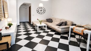 A modern living room with a checkered floor, a sofa, a coffee table, a dining table with chairs, a wall clock, and a pendant light. - Centro Storico Savona - Porto Crociere 2 (Savona)
