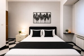 A modern hotel room with a black and white checkered floor, a bed with black and white bedding, a bedside table with a lamp, and a wall-mounted artwork. - Centro Storico Savona - Porto Crociere 2 (Savona)