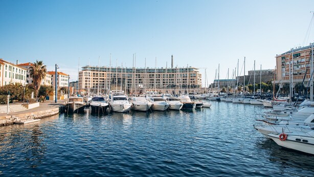 A marina with boats docked, a large building in the background, and a clear sky. - Centro Storico Savona - Porto Crociere 2 (Savona)