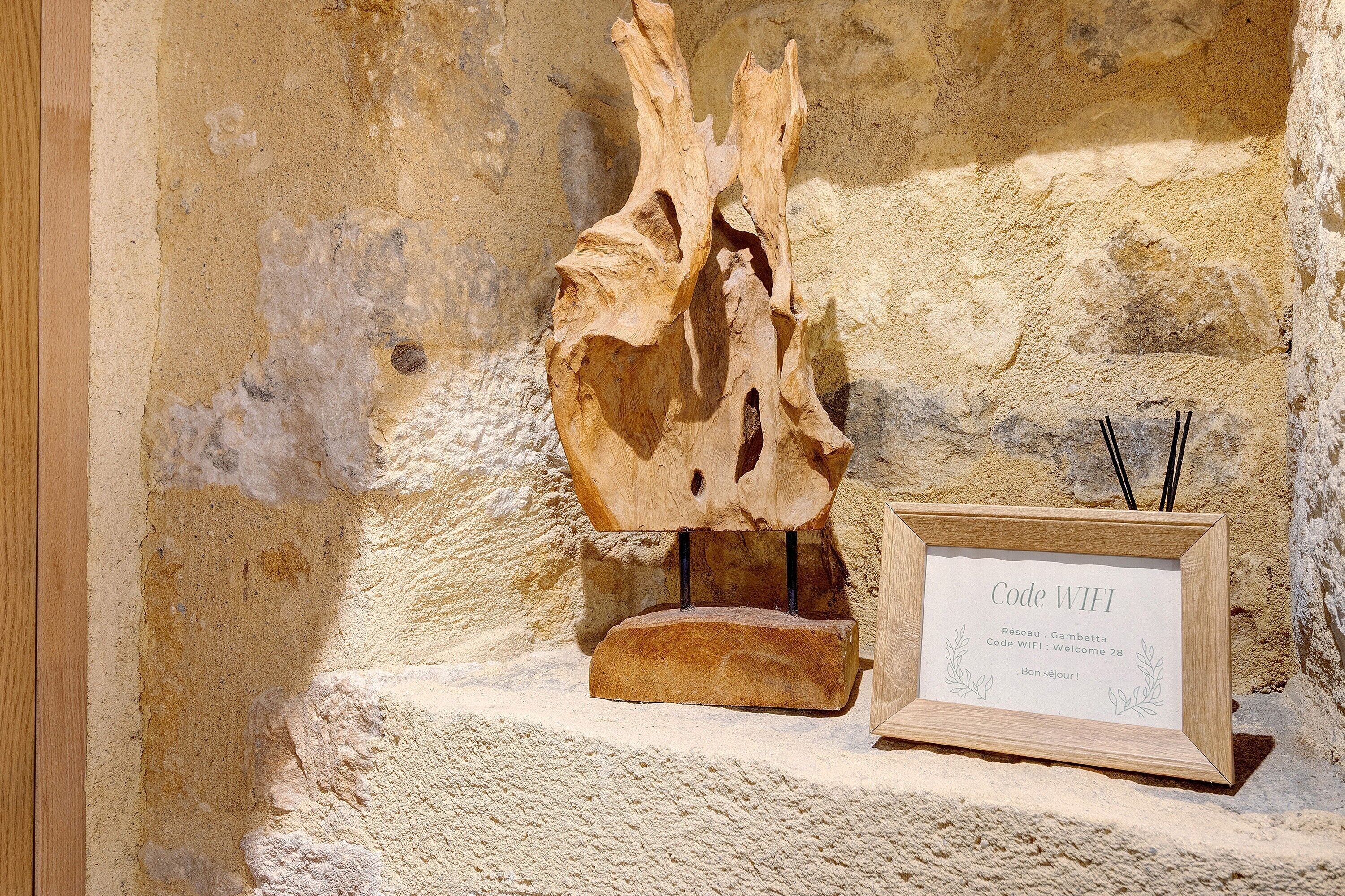 Ein Holzschild mit der Aufschrift 'Code WIFI' und 'Bienvenue 28' an einer Steinwand.
