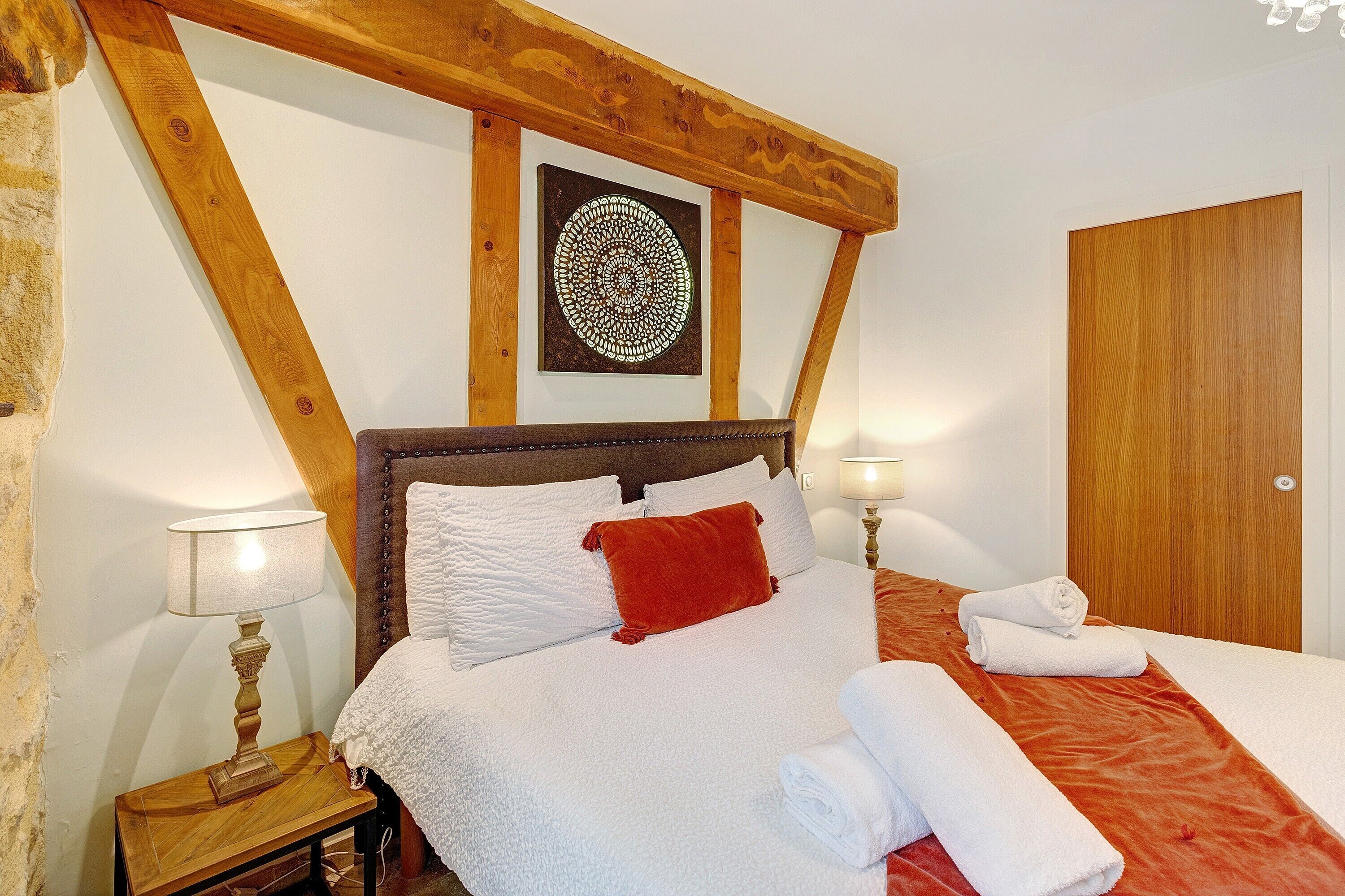 Un dormitorio con techo de madera, una cama con ropa blanca, una almohada roja y una obra de arte enmarcada en la pared.