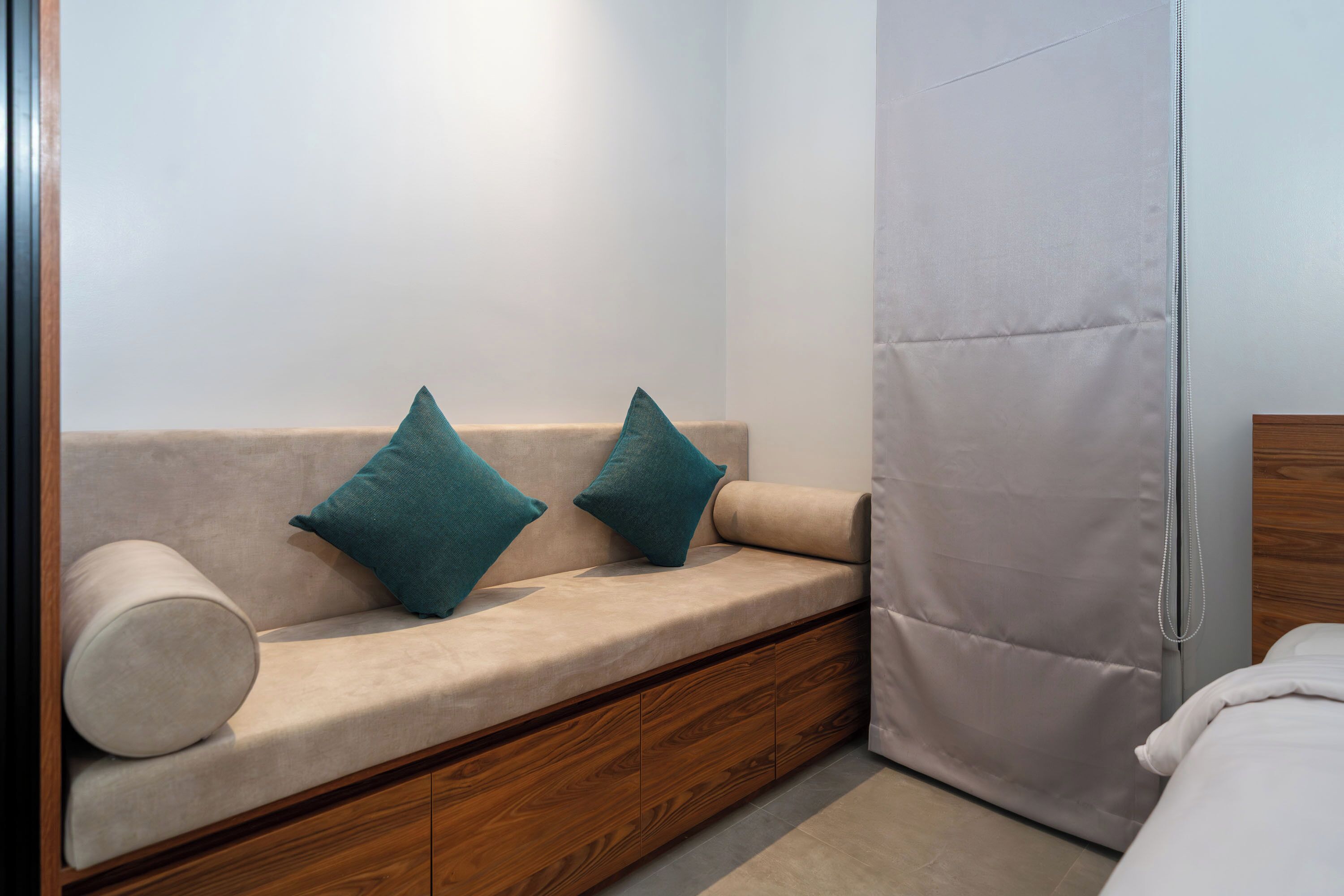 A modern room with a sofa, pillows, a wooden cabinet, and a bed.