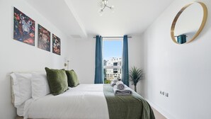A bedroom with a bed, a large window with curtains, a round mirror, and artwork on the wall. - Riverside Apartment Greenwich 2Bed Near O2 (London)