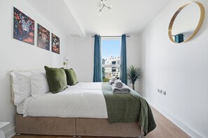 Ein Schlafzimmer mit einem Bett, einem großen Fenster mit Vorhängen, einem runden Spiegel und Bildern an der Wand.