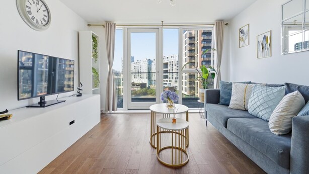 A modern living room with a flat-screen TV, a sofa, a coffee table, and a large window with a city view. - Riverside Apartment Greenwich 2Bed Near O2 (London)