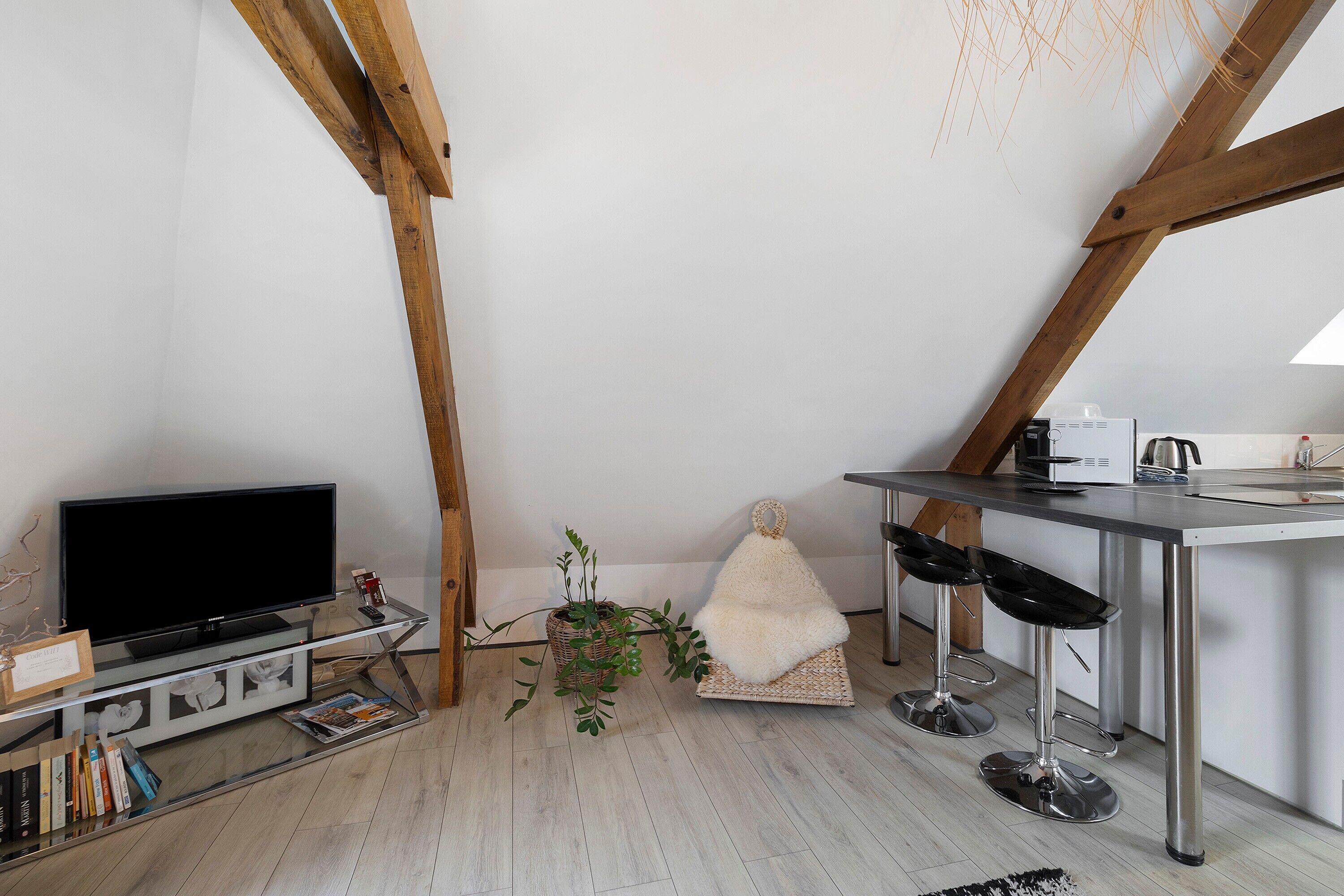 Een moderne keuken met een televisie, barstoelen, een zachte witte fauteuil en een houten plafond.