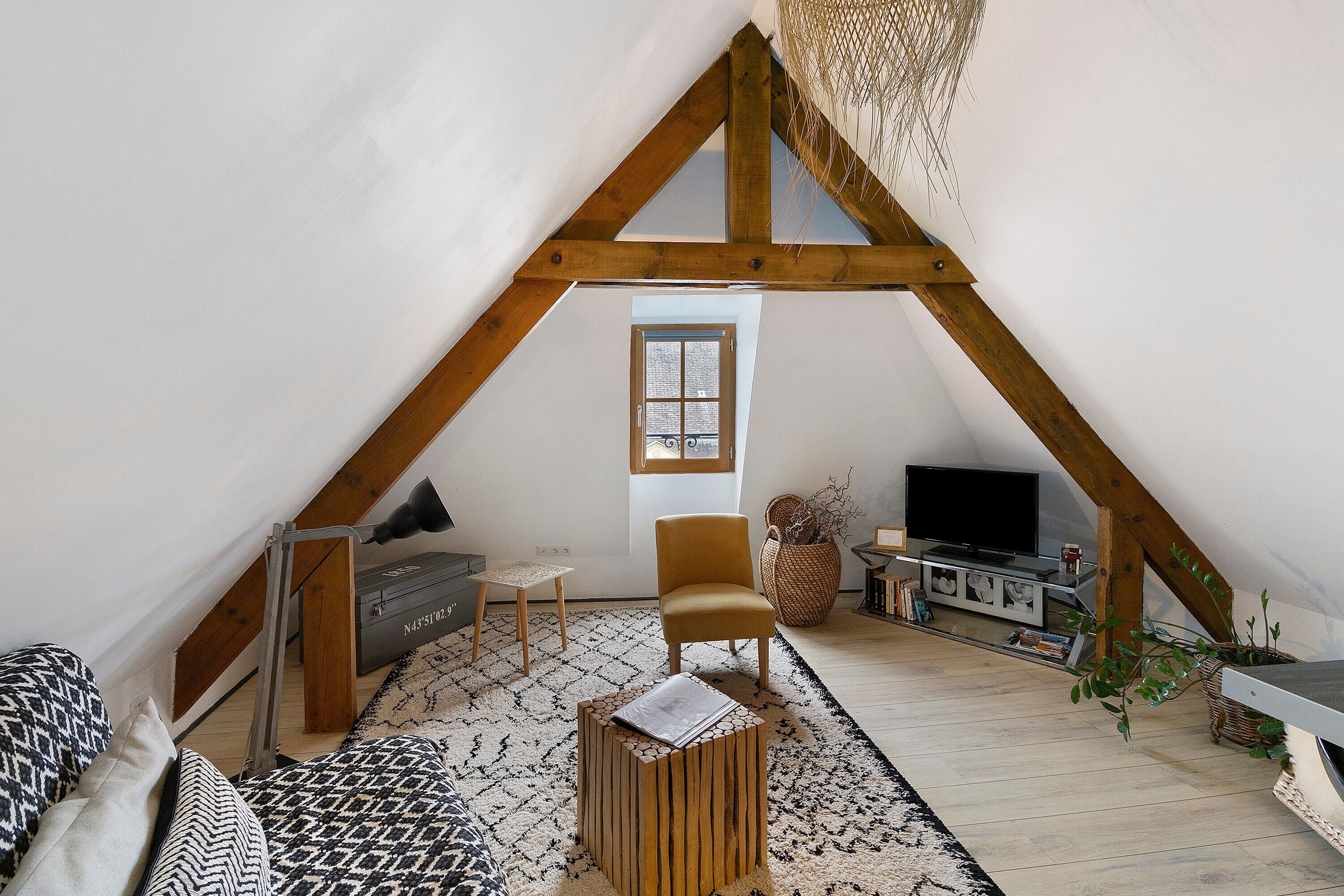 Una habitación estilo loft con techo inclinado, un televisor, un sofá, una silla y una mesita.