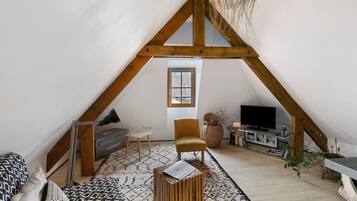 Una habitación estilo loft con techo inclinado, un televisor, un sofá, una silla y una mesita.