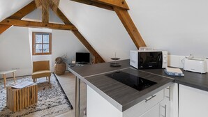 A modern kitchen with a built-in stove, microwave, and toaster. There is a wooden chair and a small table with a rug. - Charming Little Loft – WiFi, Air Conditioning, Walk to Historic Center (Sarlat-la-Canéda)