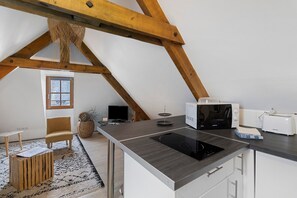 Een moderne keuken met een inbouwfornuis, magnetron en broodrooster. Er staat een houten stoel bij een kleine tafel met een vloerkleed.