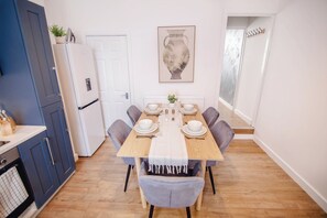 Ein Essbereich mit einem Holztisch, gedeckt für sechs Personen, umgeben von grauen Stühlen, einem weißen Kühlschrank und einem blauen Schrank.