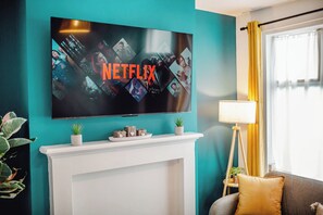 Ein Wohnzimmer mit Fernseher an einer türkisblauen Wand, Kamin, Sofa und Lampe.