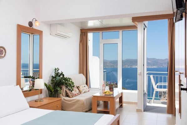 Ein Hotelzimmer mit Bett, Schreibtisch, Stuhl und einem Balkon mit Meerblick, sowie einer Klimaanlage.