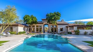 A swimming pool with a clear blue water, surrounded by a patio area with lounge chairs and a building with arched windows.