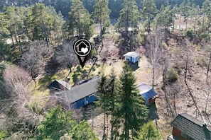 Une vue aérienne d’une propriété rurale comprenant plusieurs bâtiments, dont une maison principale et des dépendances, le tout entouré d’une forêt dense.