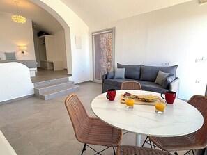 A modern living area with a round dining table, wicker chairs, a grey sofa, and a staircase leading to an upper floor. - Villa  Nira (Episkopi Gonias)