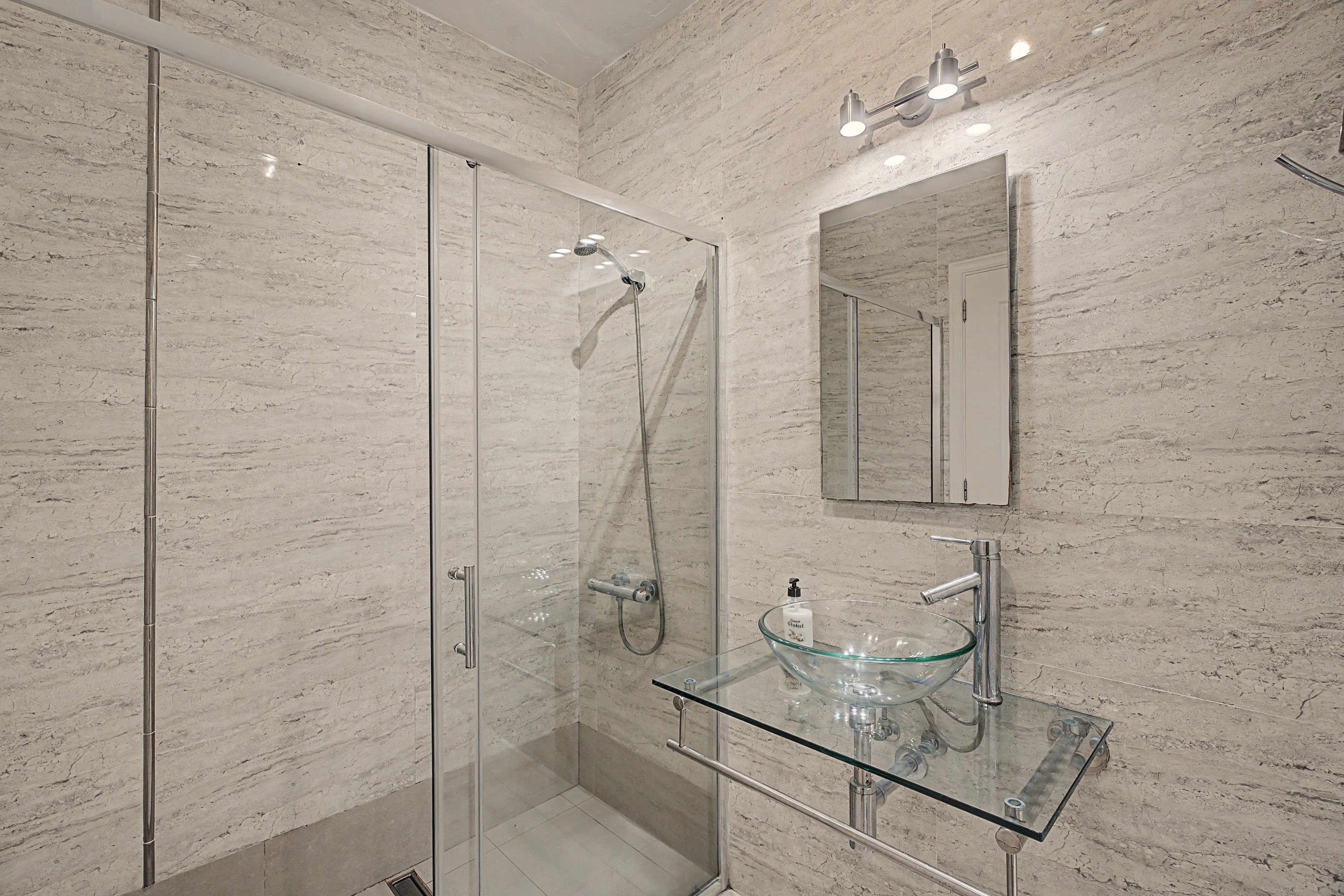 Une salle de bain moderne avec une douche à parois de verre, un lavabo en verre et un mur en marbre.