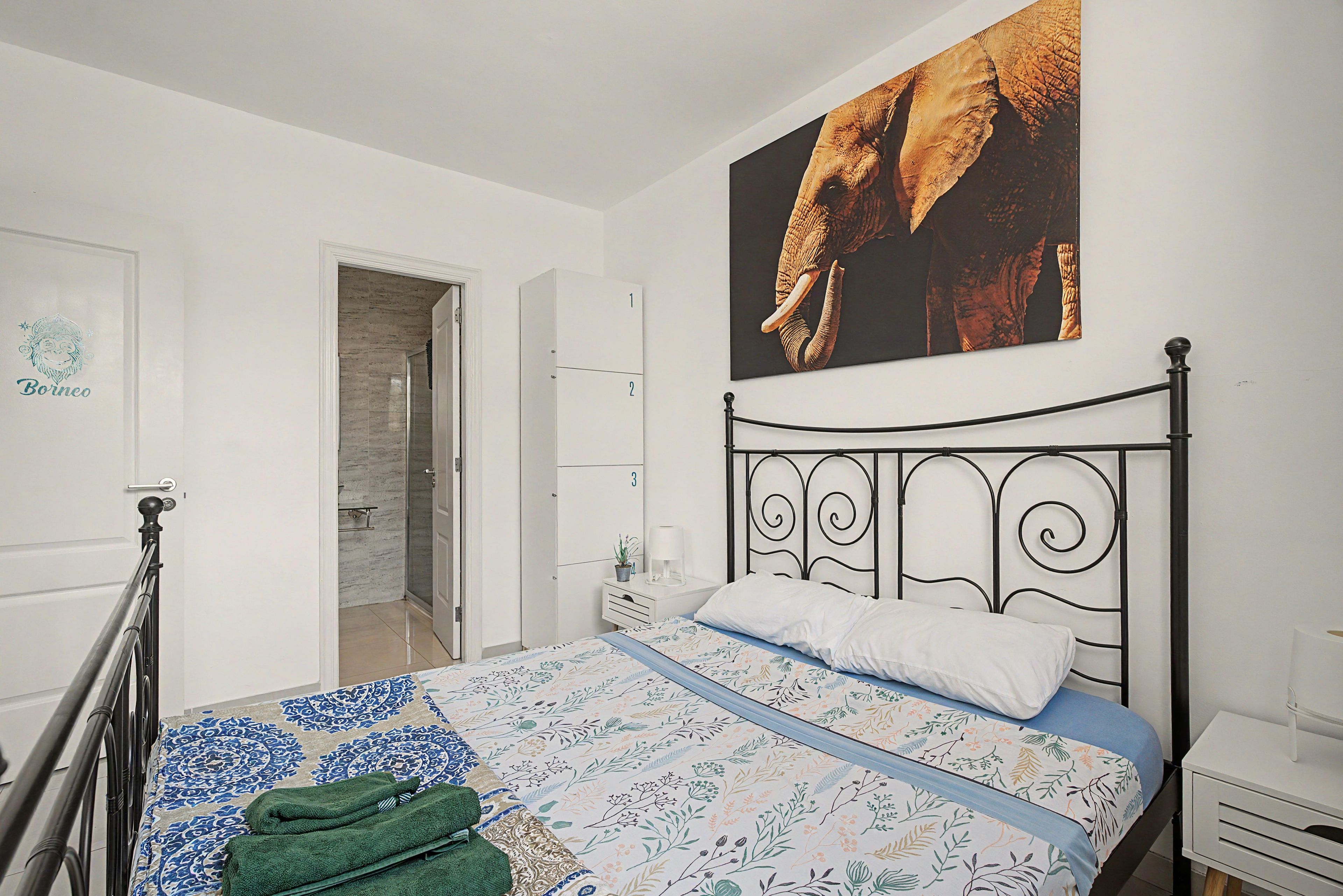 Un dormitorio con cama, una puerta, un baño y un cuadro grande de un elefante en la pared.