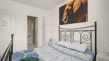 Un dormitorio con cama, una puerta, un baño y un cuadro grande de un elefante en la pared.