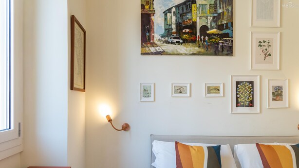 Ein Schlafzimmer mit einem Bett, einem Nachttisch, einer Wandleuchte und verschiedenen gerahmten Kunstwerken.