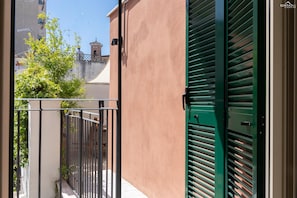 A balcony with a metal railing, a green shutter door, and a view of a building with a bell tower. - Pigneto Terrace Apartment (Rome)
