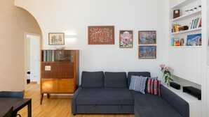 Ein modernes Wohnzimmer mit einem dunkelgrauen Sofa, einem Holzschrank und Regalen an der Wand mit Büchern und Dekoration.