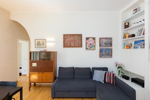 A modern living room with a dark grey sofa, wooden cabinet, and wall-mounted shelves with books and decorative items. - Pigneto Terrace Apartment (Rome)