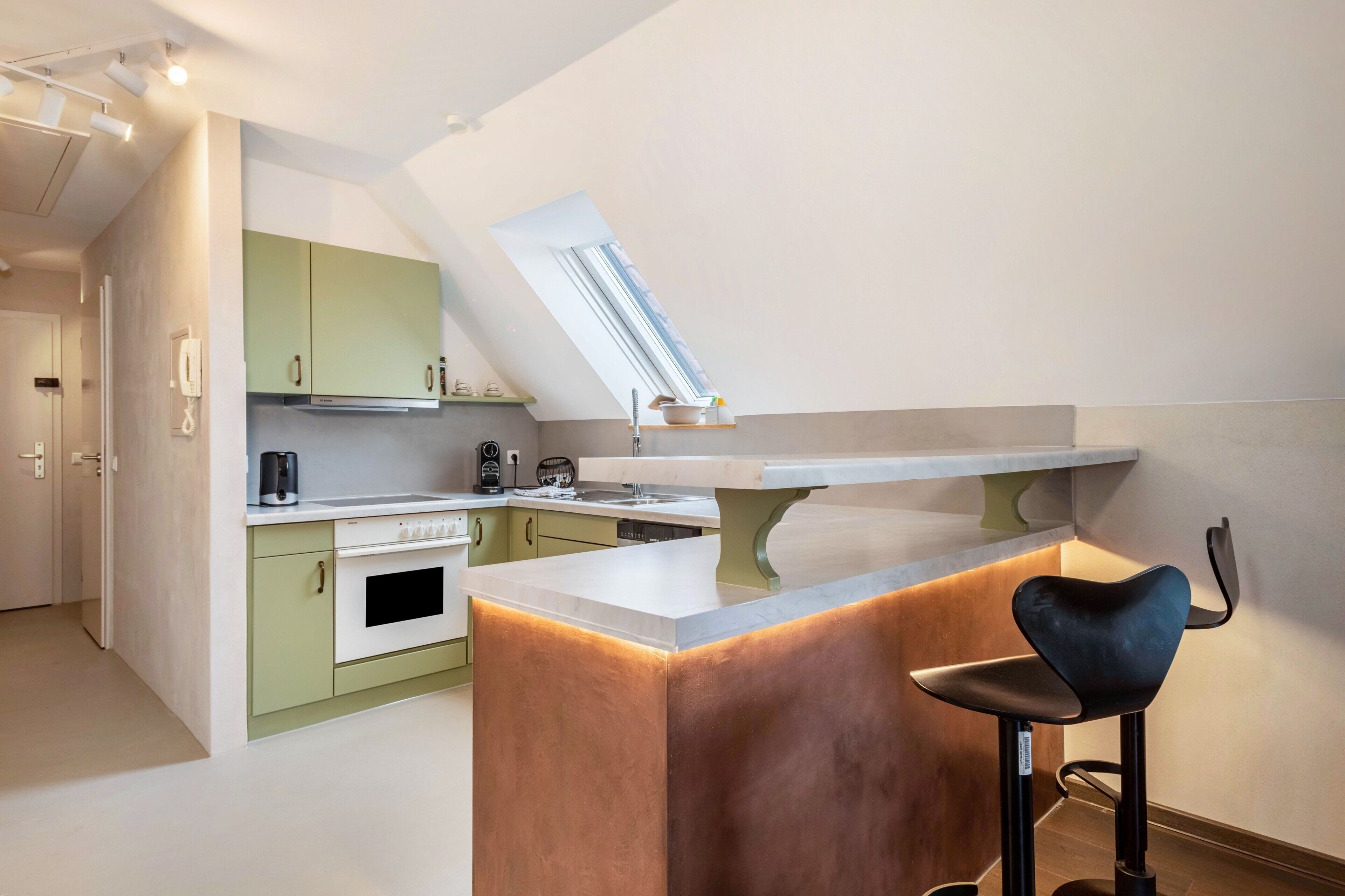Een moderne keuken met een centraal eiland, een barkruk en een dakraam.