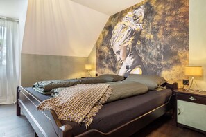 Ein Schlafzimmer mit einem Bett, einem Nachttisch, einer Lampe und einer Wand mit einem großen Gemälde.