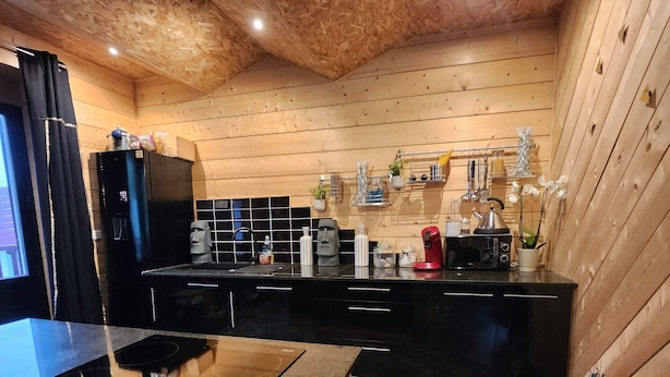 A modern kitchen with wooden walls, black cabinetry, and a central island with a stovetop. - In the heart of Font Romeu, a lovely house. (Font-Romeu-Odeillo-Via)