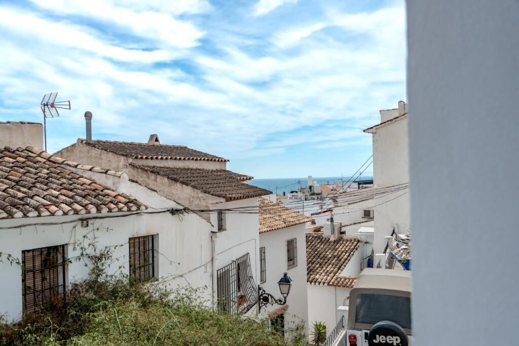 Une rue étroite bordée de bâtiments traditionnels, un véhicule Jeep bien visible et un ciel dégagé.